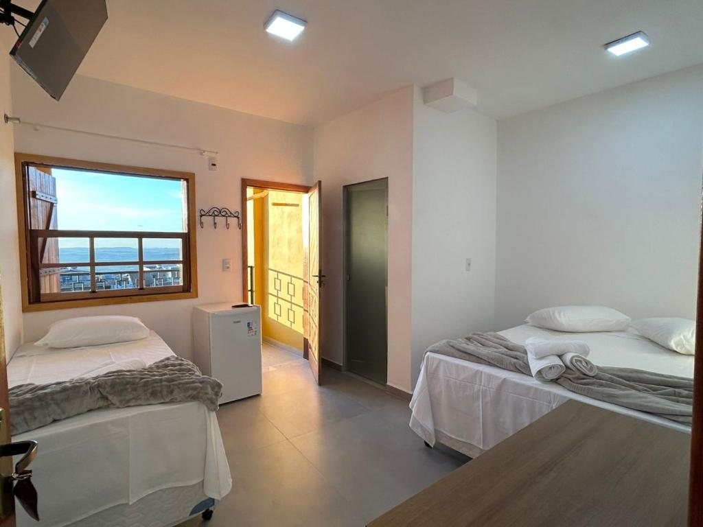 Quarto claro com duas camas e janela de madeira aberta para a paisagem